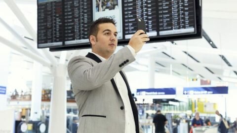 a man holding his phone up to a sign in the airport