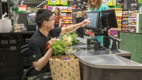 Image of a staff member in a wheelchair at Woolworths happily serving a customer.